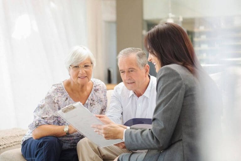 An older adult man and woman sit with a younger woman, who is showing them some paperwork on a clipboard.