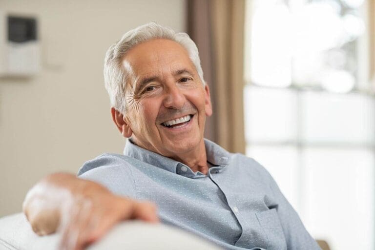 An older adult is sitting and smiling at the camera.