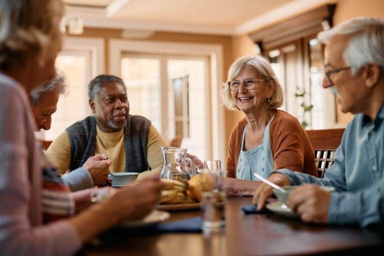 Two older adult women and three older adult men sit at a table to enjoy a meal together.