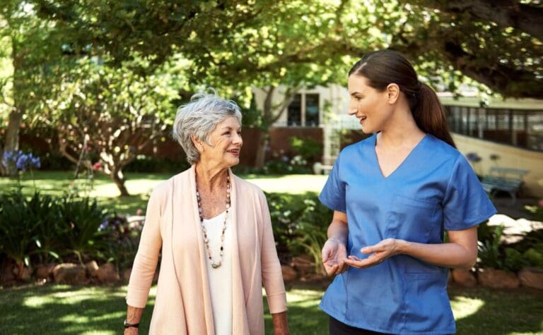 An older adult woman is outside standing with a younger woman wearing scrubs.