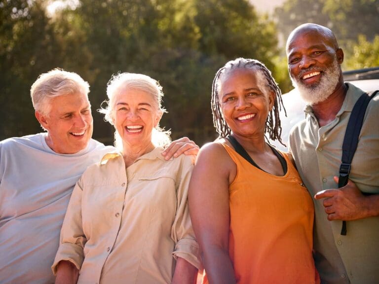 Two older adult men and two older adult woman are standing outside, smiling at the camera.