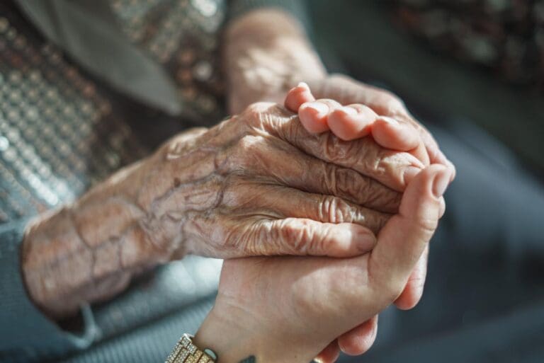 An older adult woman's hands are shown holding a younger person's hand.
