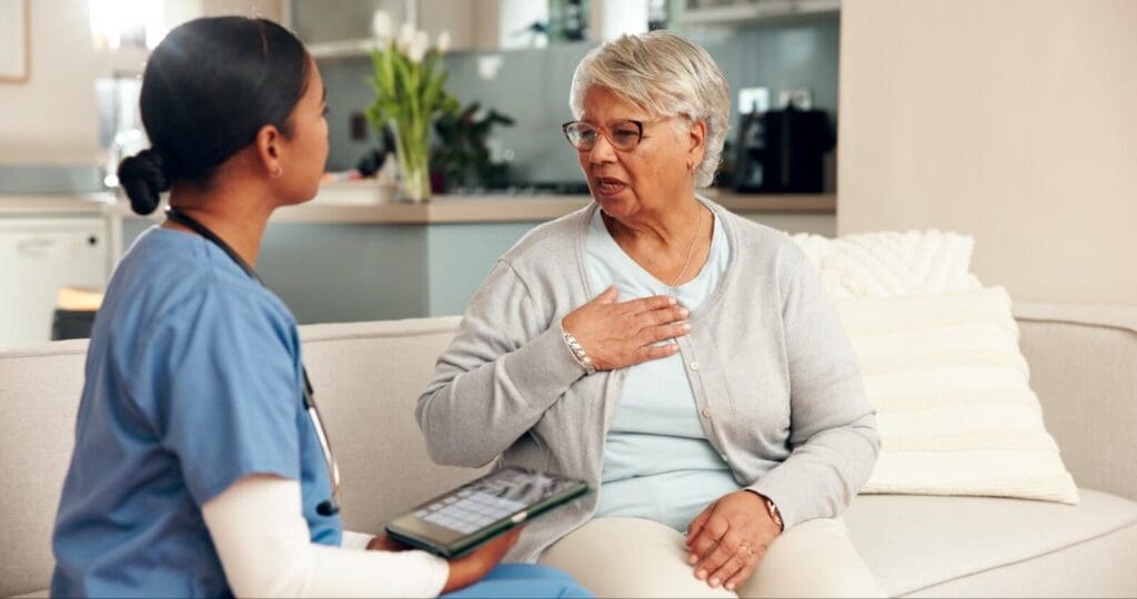 An older adult woman sits on her couch talking with a female health care worker.