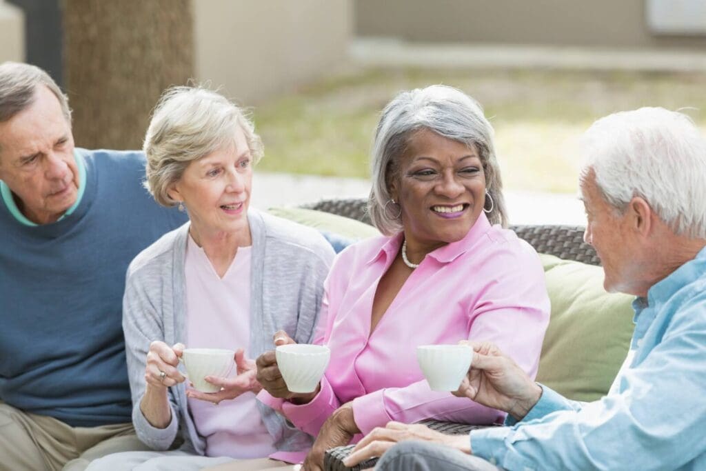 A group of two older adult women and two older adult men are sitting on a couch, drinking tea and chatting.